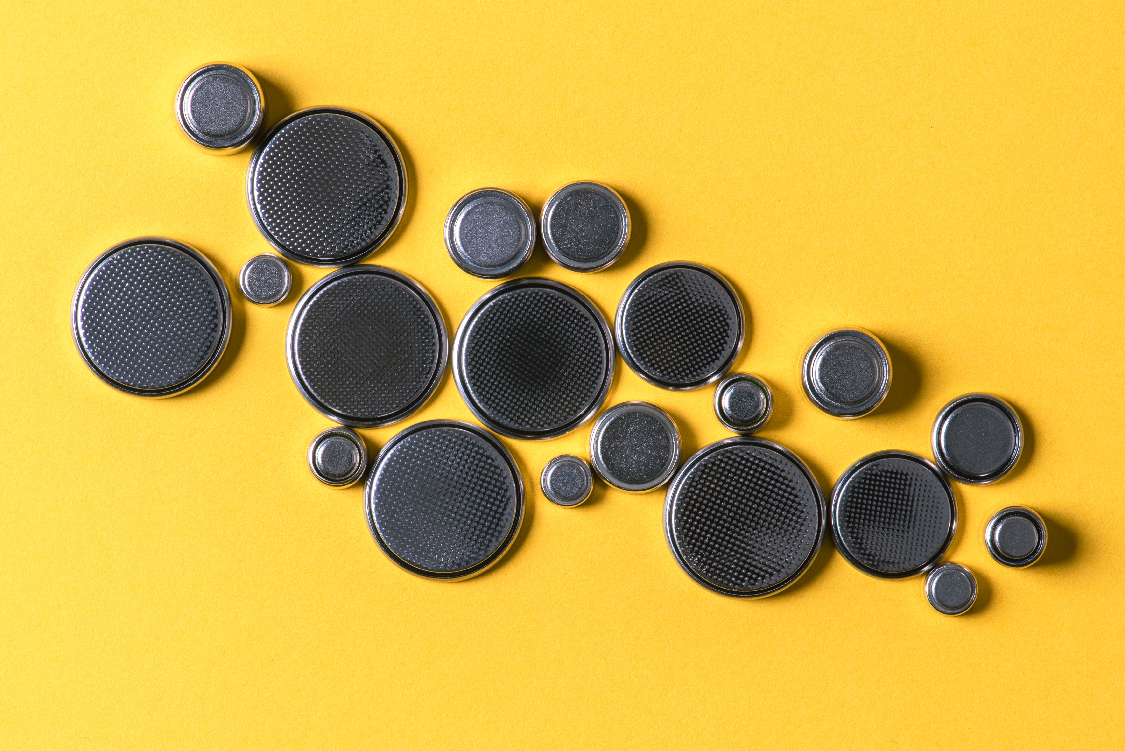 Button batteries of various sizes laid out on a yellow table. 