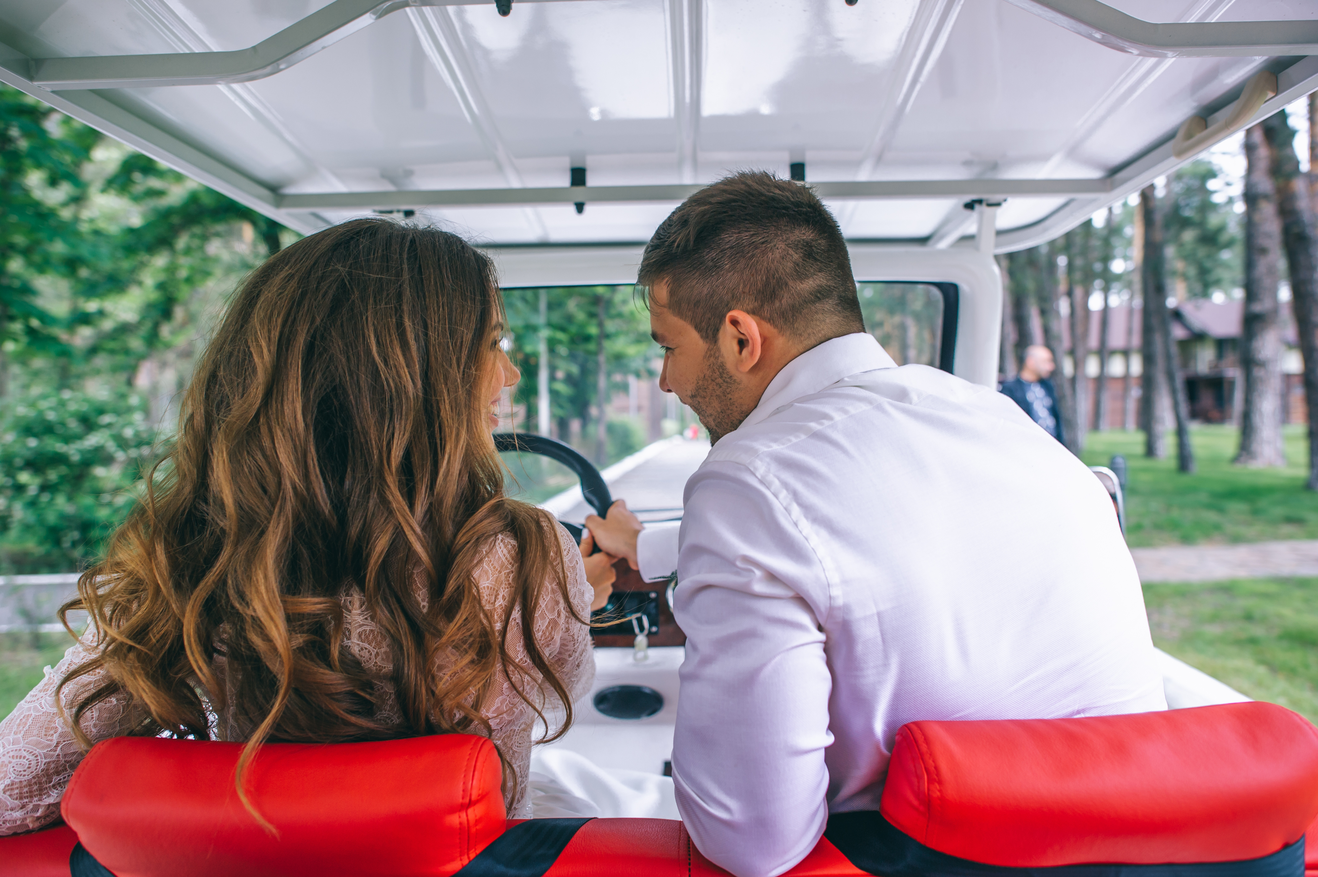 woman and a man sitting in a golf cart. the camera is behind them, so you can only see the back of their heads