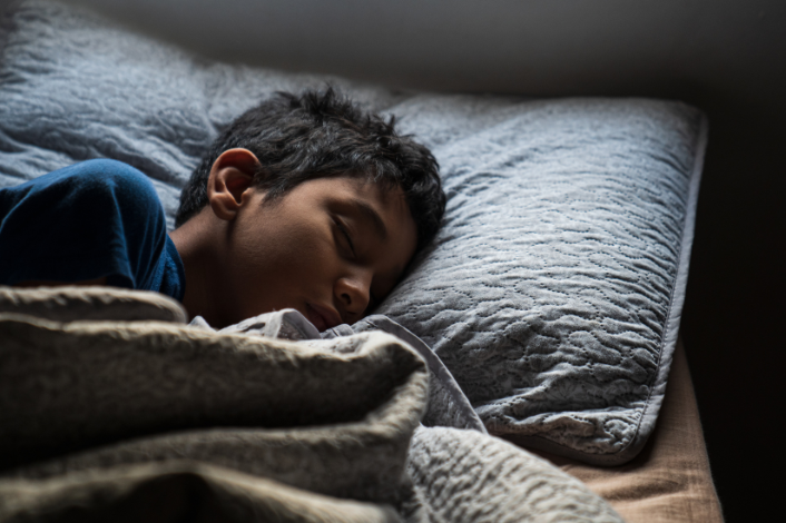 young boy sleeping in his bed covered up by a blanket