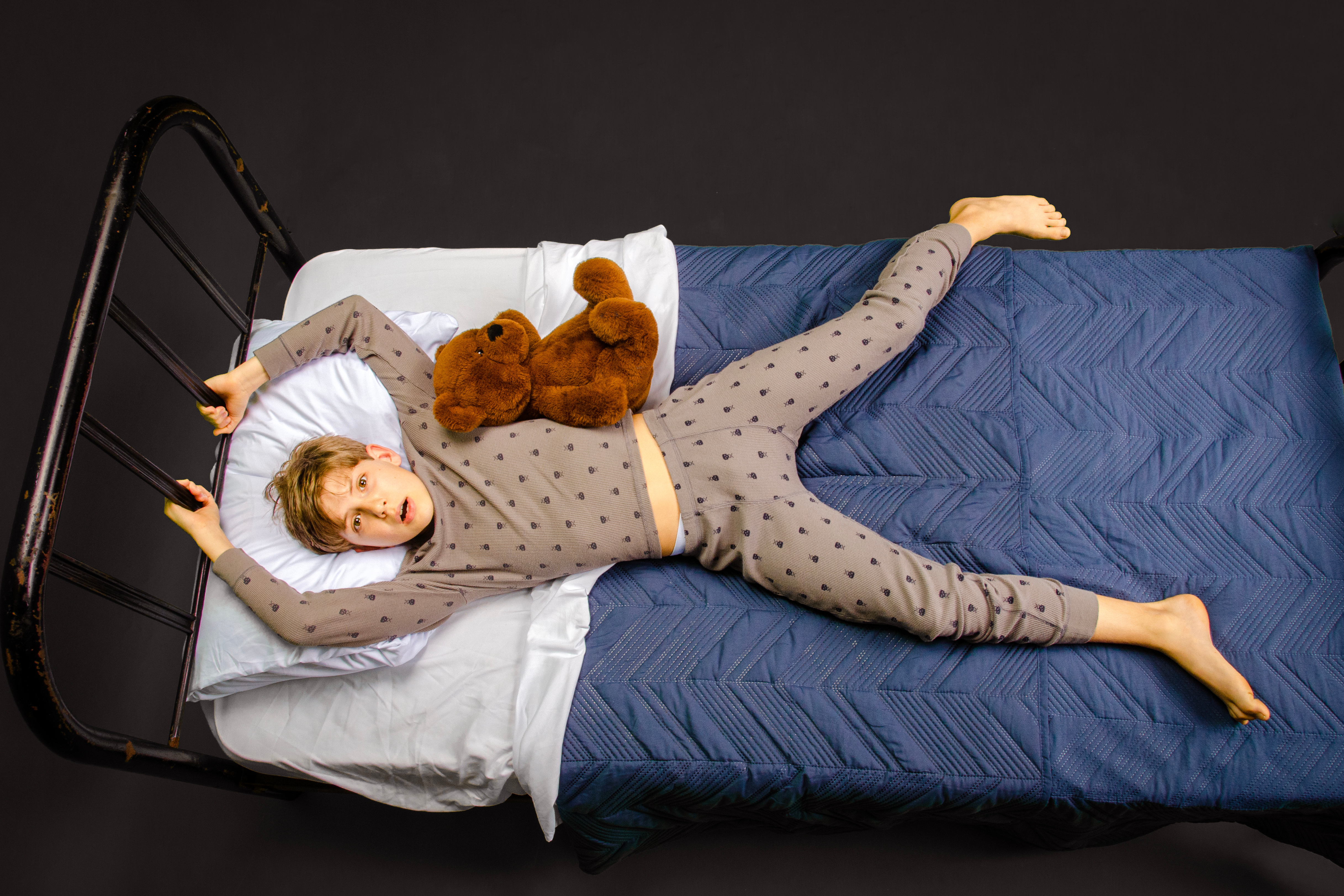 Young boy laying on a bed with his hands around the headboard.