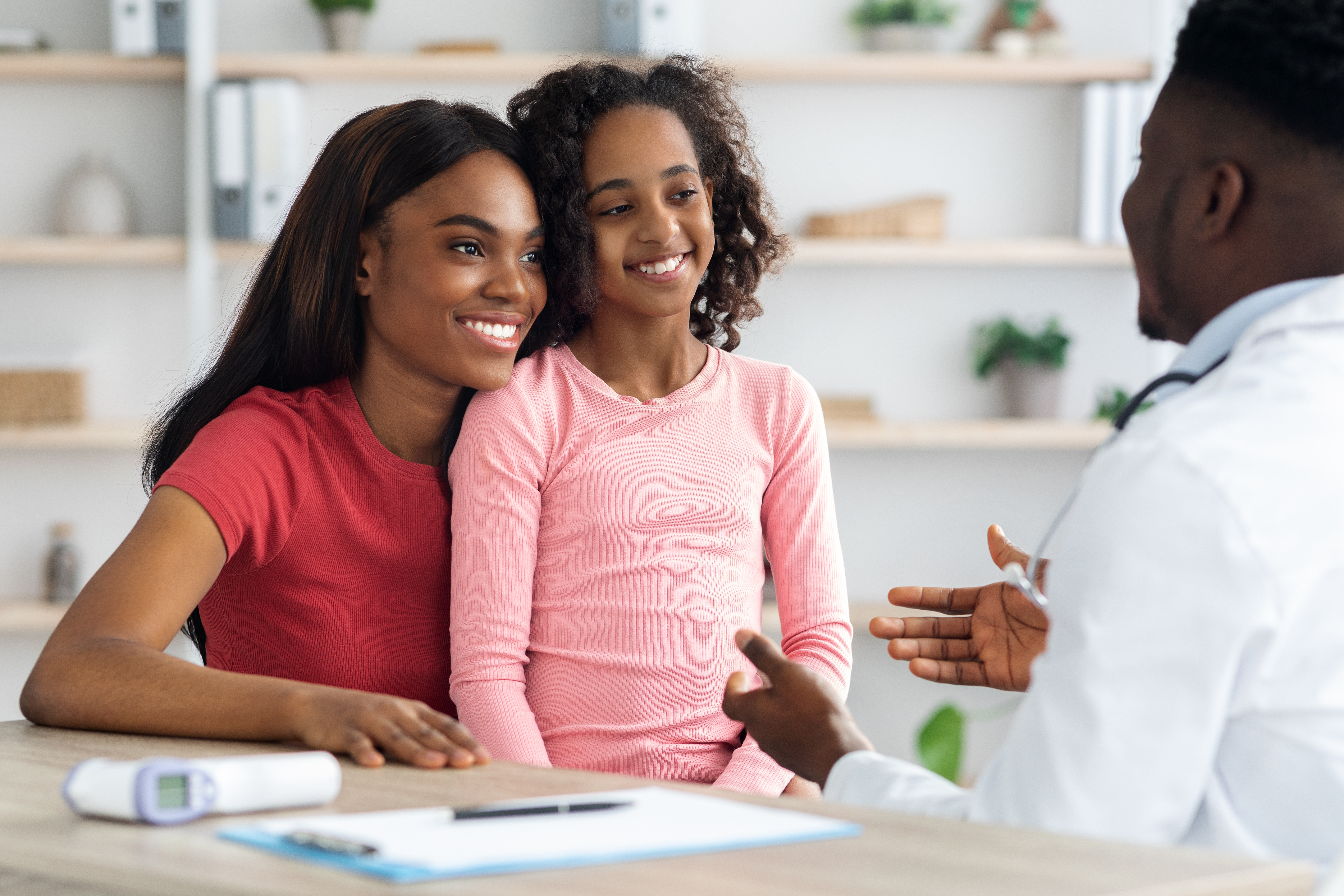 A mother and daughter smile while speaking with a doctor across a desk, engaged in a warm, supportive healthcare conversation