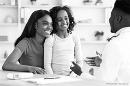 A mother and daughter smile while speaking with a doctor across a desk, engaged in a warm, supportive healthcare conversation