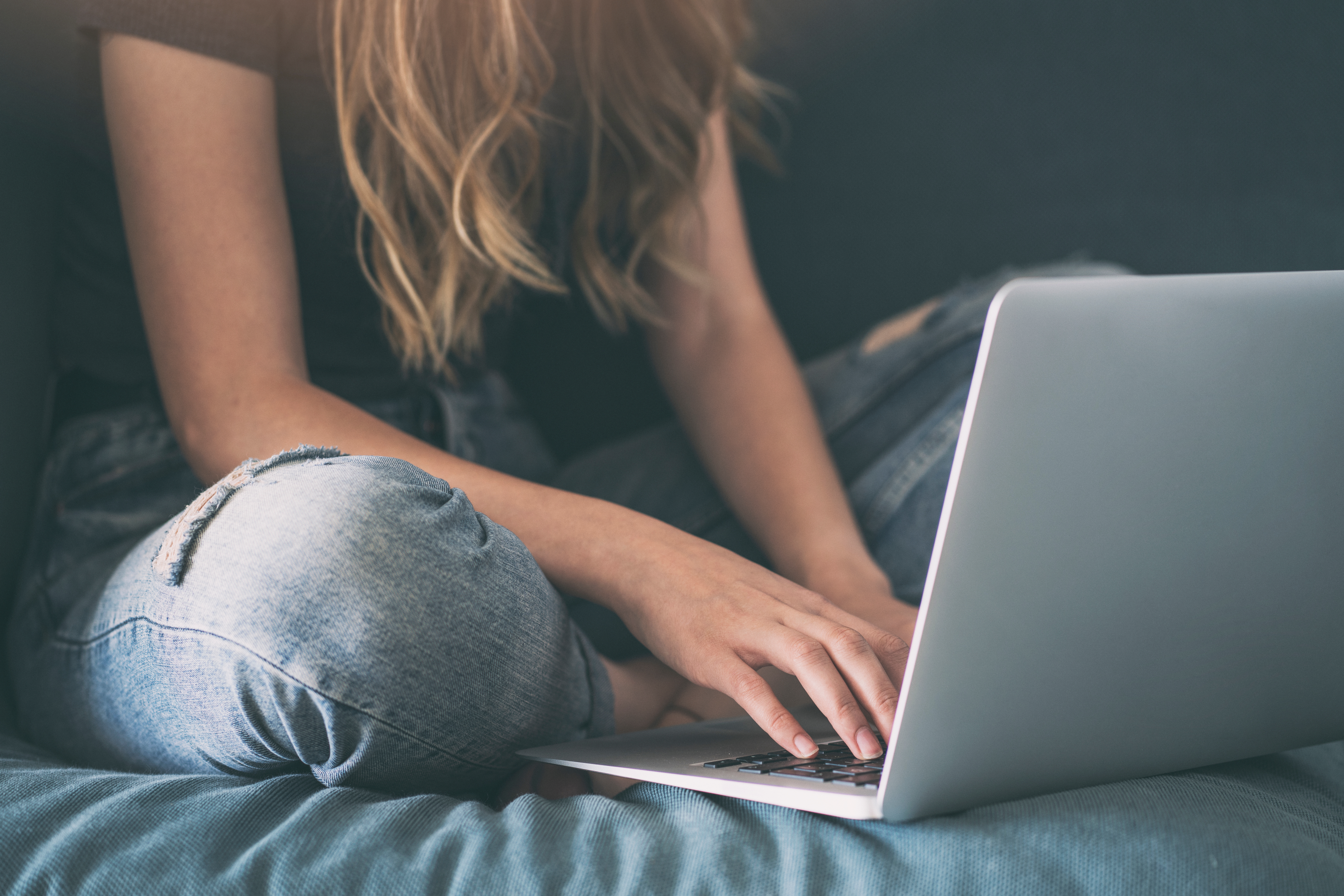 A teenage girl is sitting on a bed with a laptop in front of her.