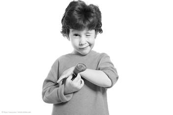 Black and white image of toddler-aged boy with short dark hair holding a watch and winking at the camera.