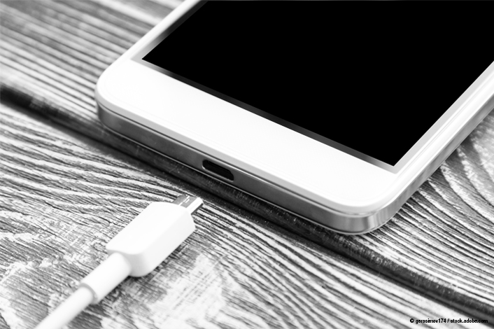 Close-up of a smartphone lying on a wooden surface with a USB charging cable positioned near the charging port, ready to be connected.