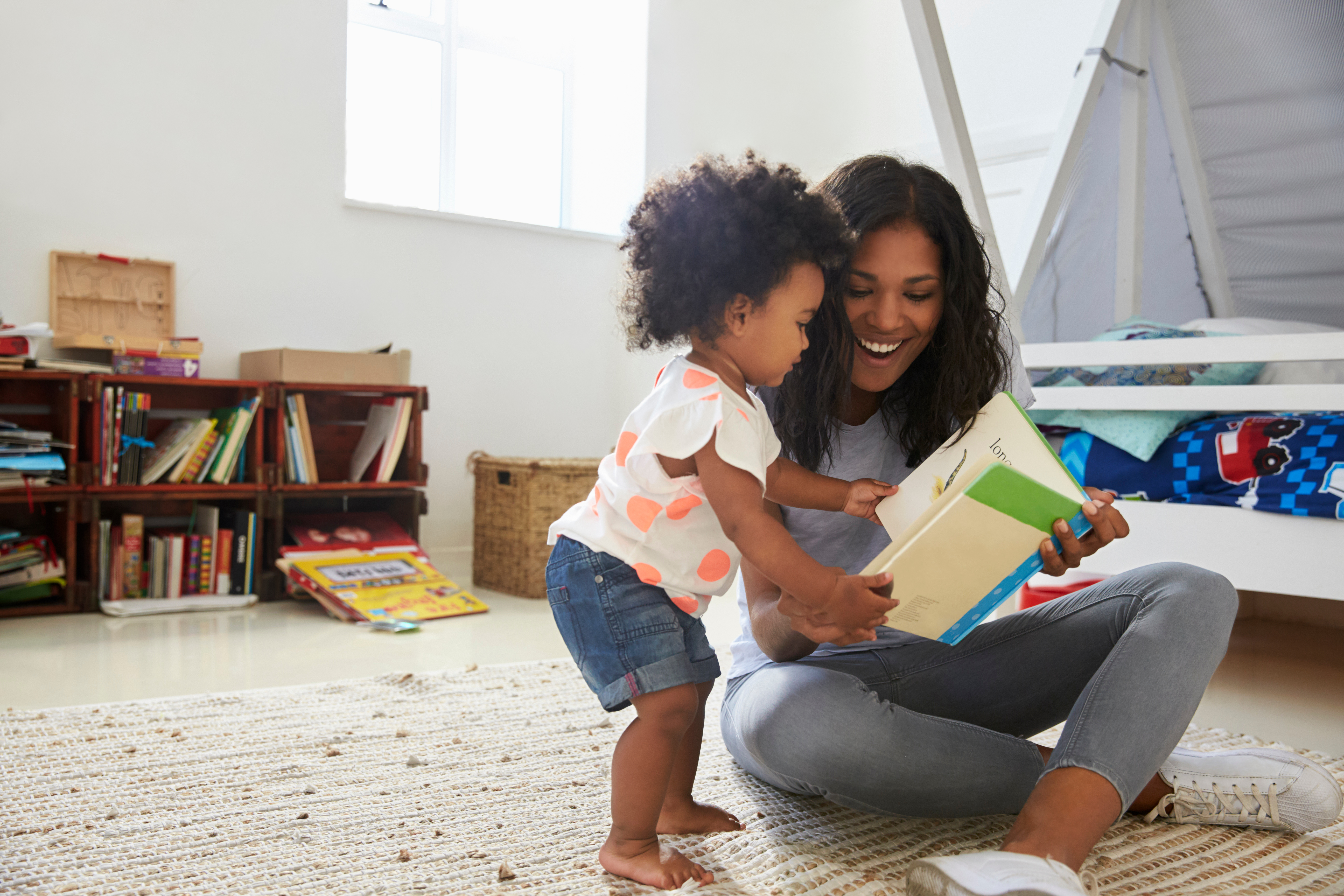 mother sitting on the floor reading a book to her toddler