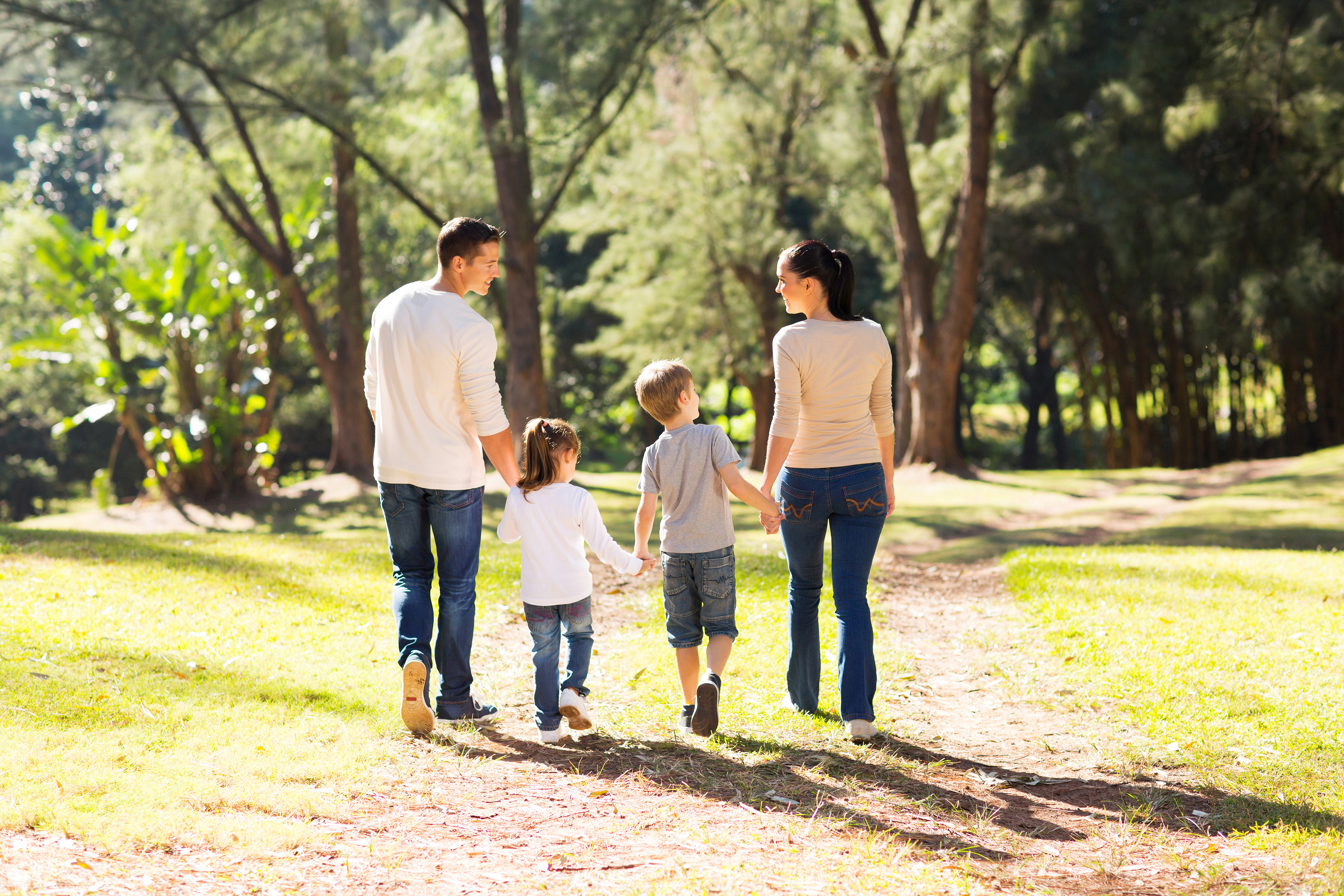 Family of four, 2 parents and 2 kids, holding hands walking in a park