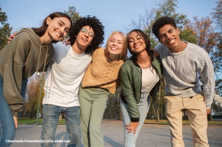 A group of teens posing with their arms around each other smiling at the camera.