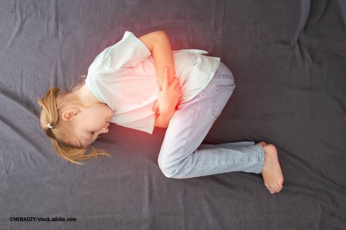 A young girl lies curled on her side on a bed, holding her lower abdomen in discomfort. A red glow highlights the stomach area, illustrating abdominal pain commonly associated with illness or infection.