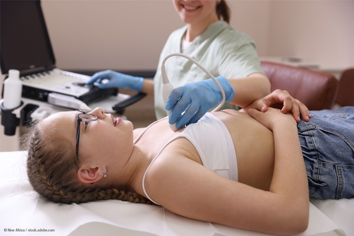 A healthcare professional performs an ultrasound examination on a teenage patient lying on an exam table. The patient wears glasses and rests comfortably while the clinician uses an ultrasound probe on the upper abdomen, illustrating a pediatric cardiology or diagnostic imaging visit.