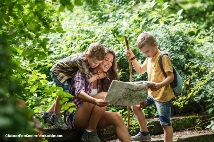 Mother and her little sons hiking. They are taking a break and sitting on the old stairs. Examining map.
