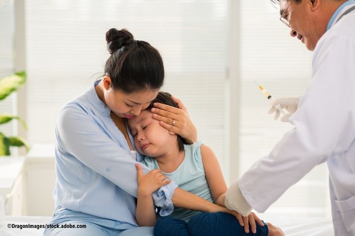 Mother holding their child to their chest while a doctor holds a needle near them. 