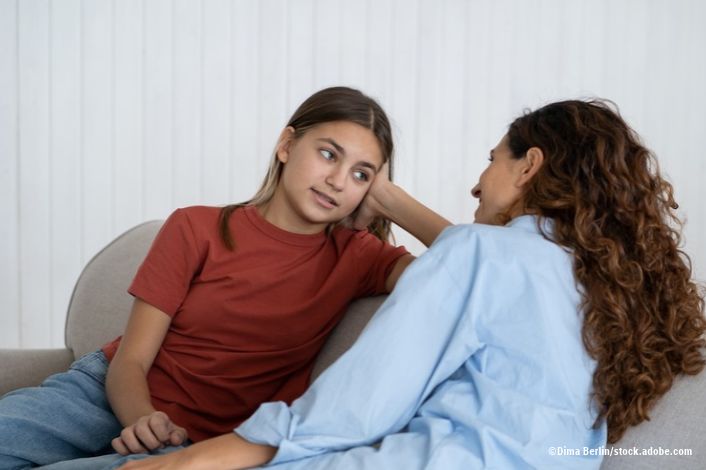 Relaxed optimistic woman and school age girl talking and sharing secrets sits on sofa indoors. Casual mom and teenage daughter with slight smile talk about important topics and discuss child friends by DimaBerlin