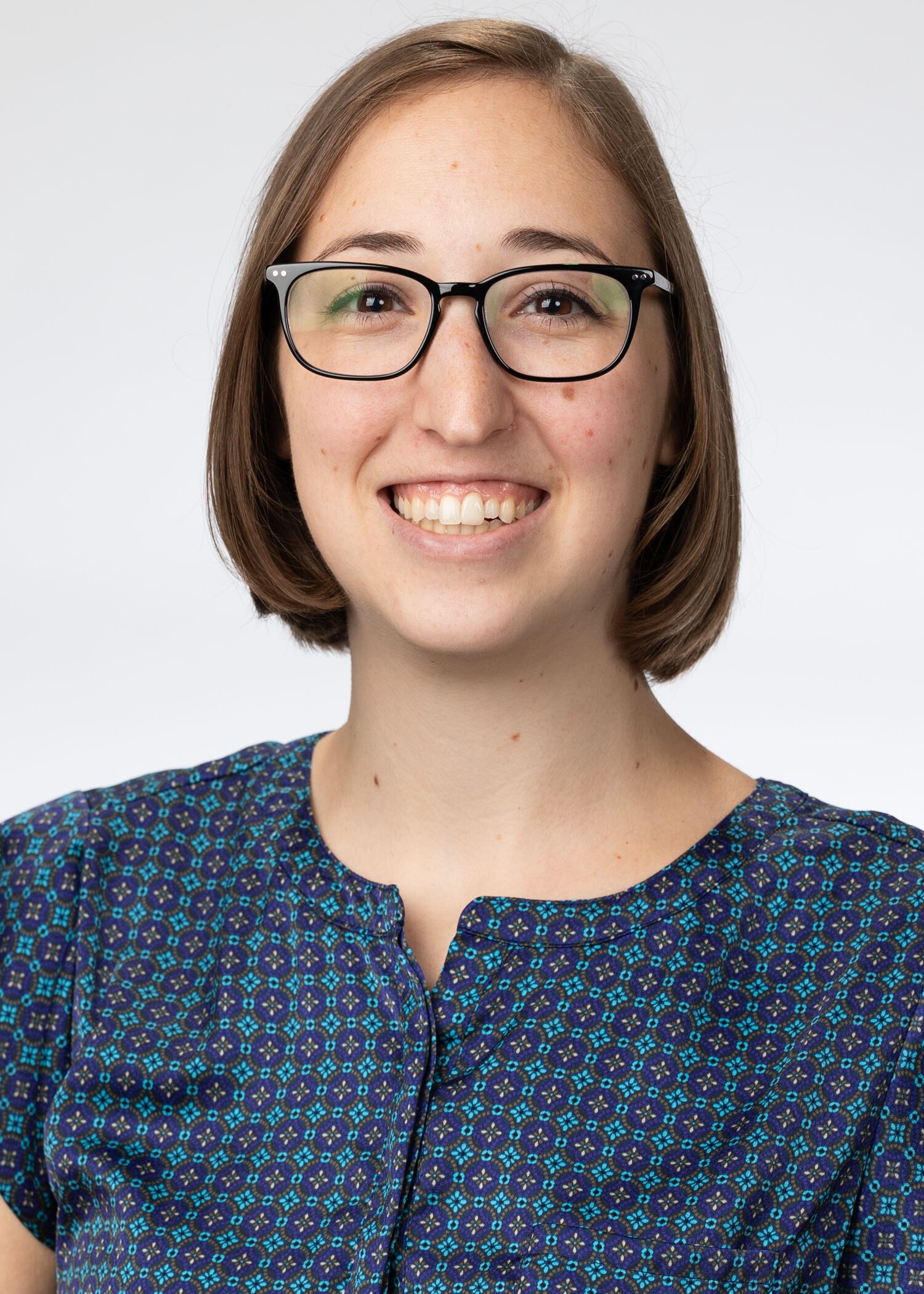 Portrait of Madison Hoenle, woman with short brown hair, glasses, and a blue shirt.