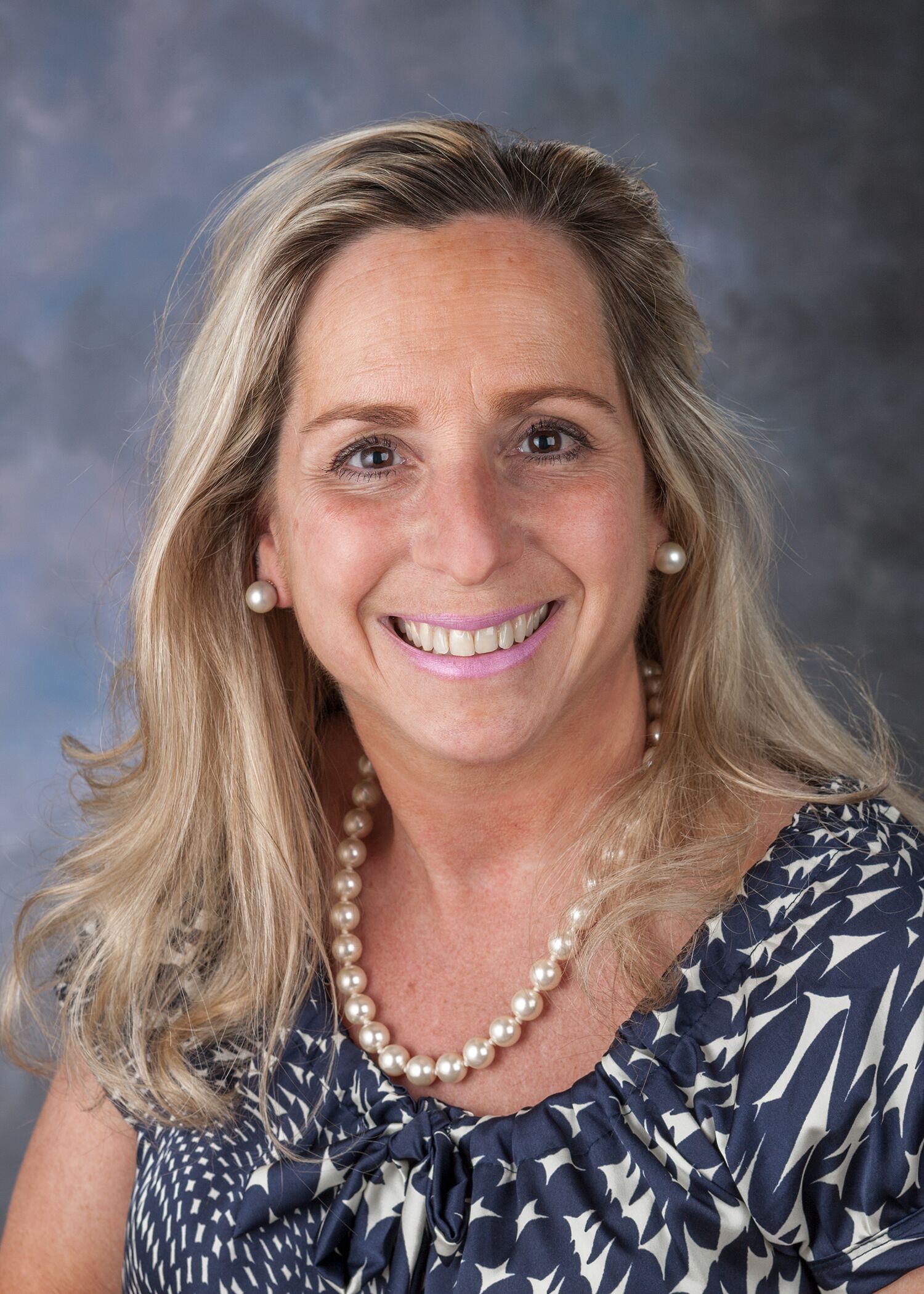 Portrait of Marcie Rehmar, woman with long blonde hair and a black patterned shirt.