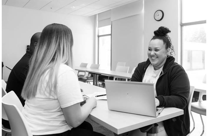 A smiling woman is seated in front of a laptop and a couple. She's ready to assist them with their taxes.
