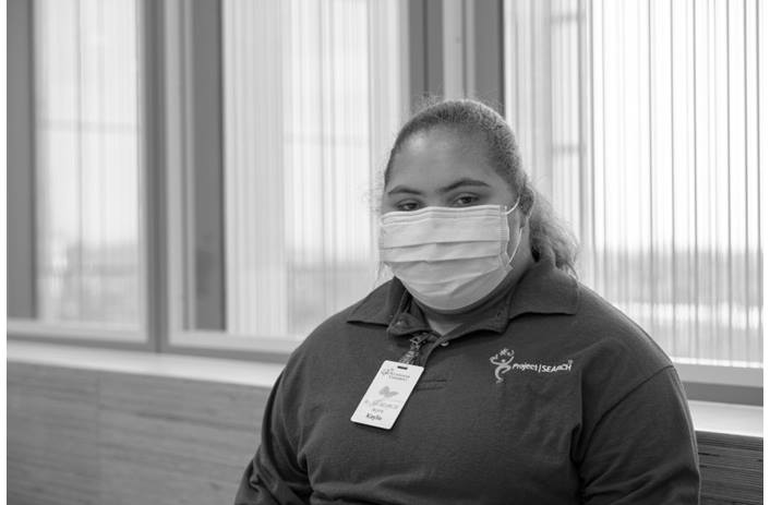 Project SEARCH participant, wearing a mask, standing near a wall of windows
