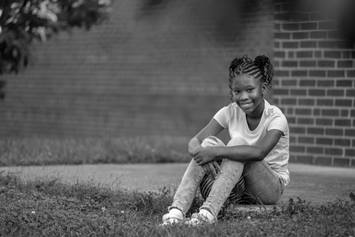 Elementary aged student, sitting in the grass, smiling