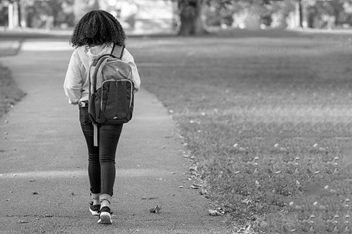 A teenage girl is walking on an outdoor path. She is wearing a back pack.