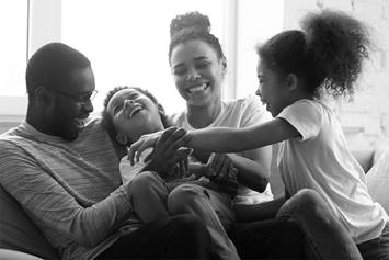 A mom, dad and two children are shown sitting on a couch, laughing