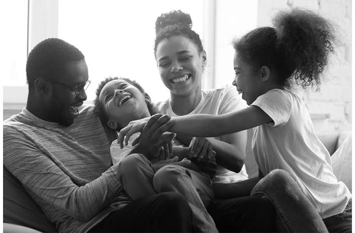 A mom, dad and two children are shown sitting on a couch, laughing