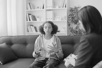 A pre teen age girl sits on a couch, with a woman intently listening across from her.