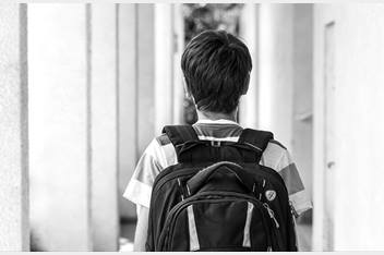 Teenage boy is wearing a backpack and walking down a hallway