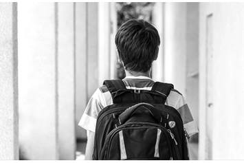 Teenage boy is wearing a backpack and walking down a hallway