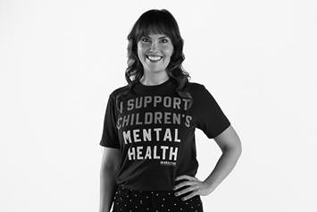 Dr. Hoet is wearing an "I Support Children's Mental Health" shirt. She's smiling with her left hand resting on her hip.