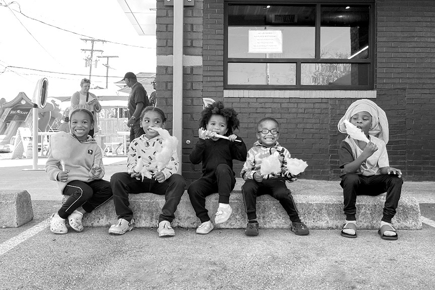 A group of kids are seated on a sidewalk, happily snacking on cotton candy.