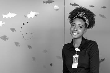 Makayla is smiling, standing in front of a glass privacy wall with fish graphics on it