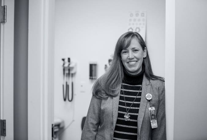 Mary Kay Irwin is smiling and standing in a school-based health service clinical area.