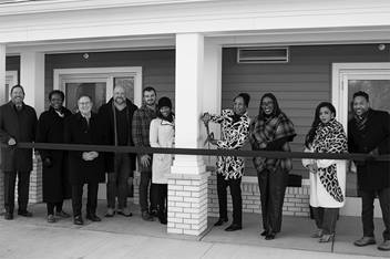 A group of individuals cutting a large ribbon in front of a building.