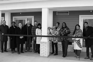 A group of individuals cutting a large ribbon in front of a building.