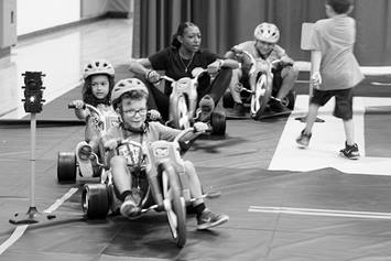 Elementary aged children practice riding bikes in a gymnasium setting.