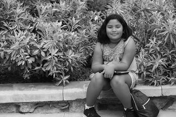 An elementary aged girl is sitting on a bench with her back pack next to her.