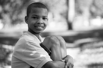 Elementary aged boy is sitting outside, hugging his knees to his chest, smiling