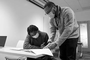 An employee is standing next to a seated individual. They are looking through tax documents together.