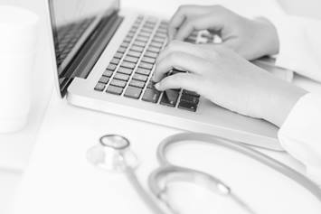 Adult typing on a keyboard with stethoscope sitting on the desk top nearby