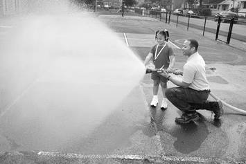 A firefighter shows an elementary aged girl how to use the fire hose