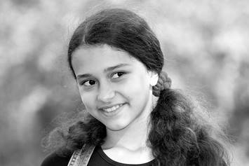 Close up of a smiling elementary aged girl with curly hair styled in two ponytails