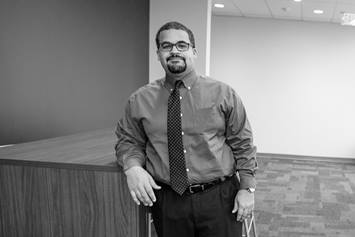 Nick Jones is standing in an office building, resting his elbow on a high-top table