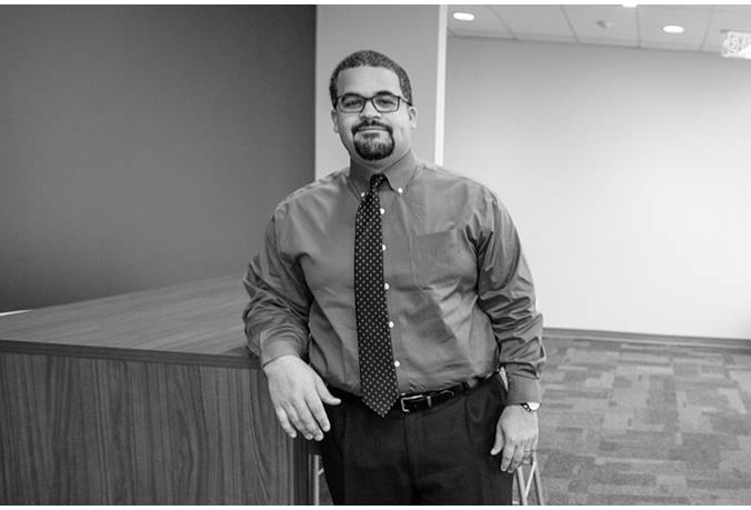 Nick Jones is standing in an office building, resting his elbow on a high-top table
