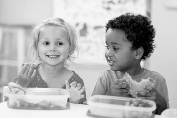 A preschool-aged girl and boy are eating lunch at a table