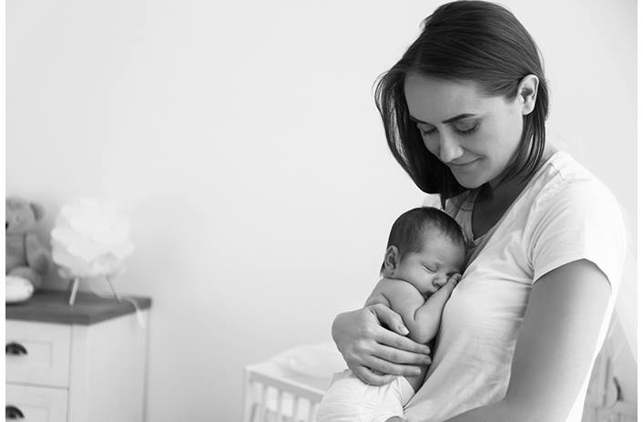 A smiling mom embraces her newborn baby