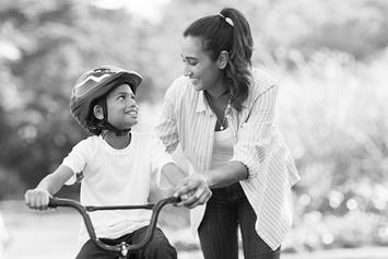 A mom is helping her son ride his bicycle