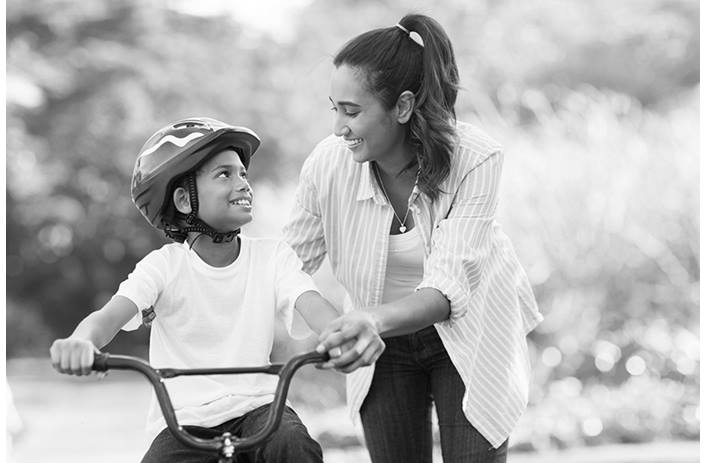 A mom is helping her son ride his bicycle