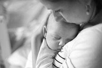 A mom embraces her young baby in her arms as she kisses its forehead