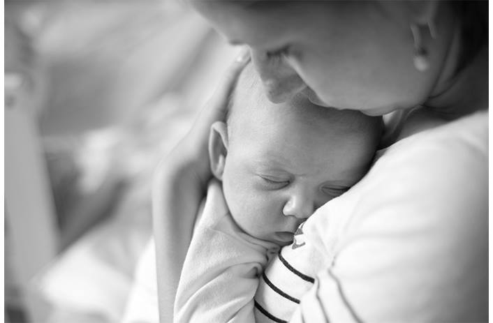 A mom embraces her young baby in her arms as she kisses its forehead