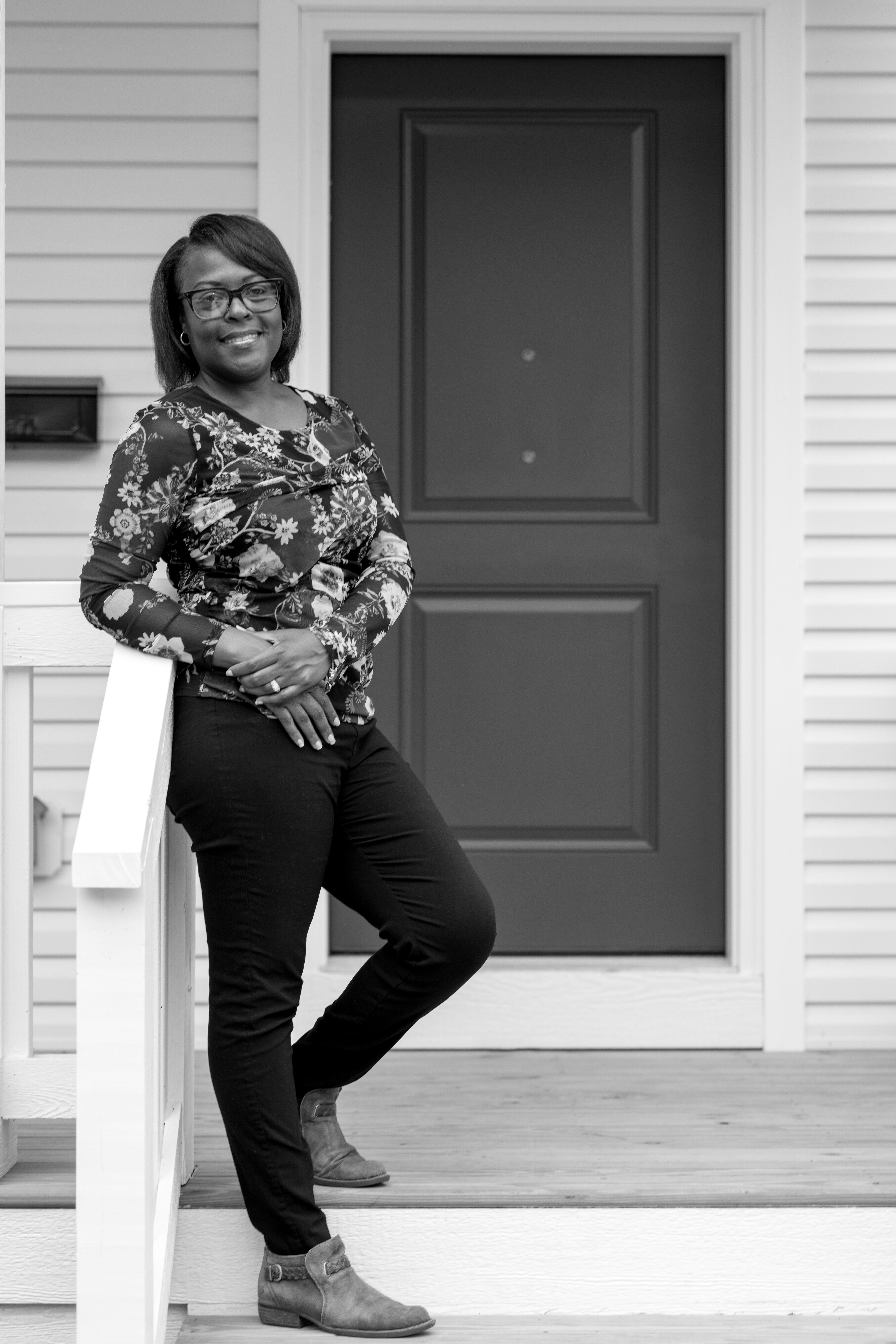 Sheryl is wearing a printed long sleeve shirt and dark pants. She's standing on a front porch, smiling.